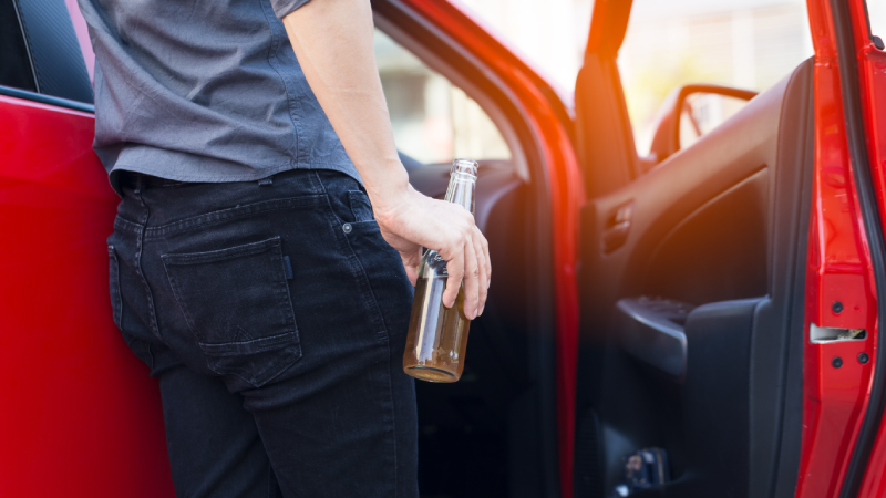 close up of Man hand holding alcohol bottle already driver and drinking alcohol from a bottle as a driving the car,dangerous concept