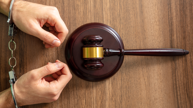 Handcuffed Convict, Law offender and Justice. Court sentence Prison. Handcuff locked and judge gavel on a wooden table, top view.