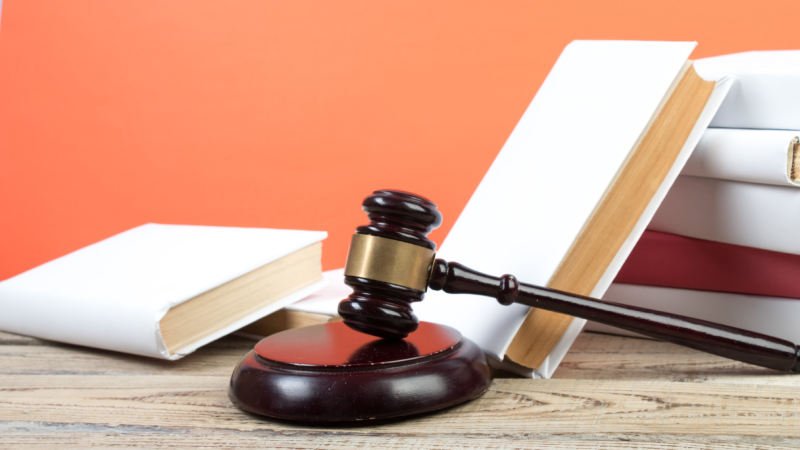 Law concept - Open law book with a wooden judges gavel on table in a courtroom or law enforcement office on blue background. Copy space for text