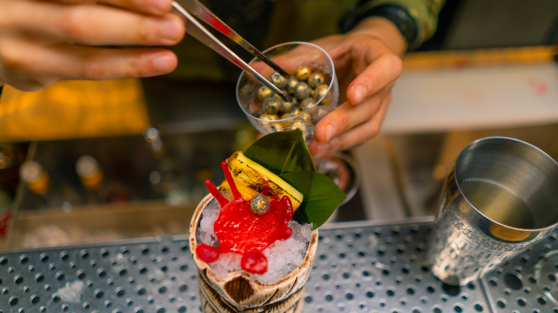 a bartender in a bar or restaurant decorates a freshly prepared alcoholic cocktail lays out decor with tongs