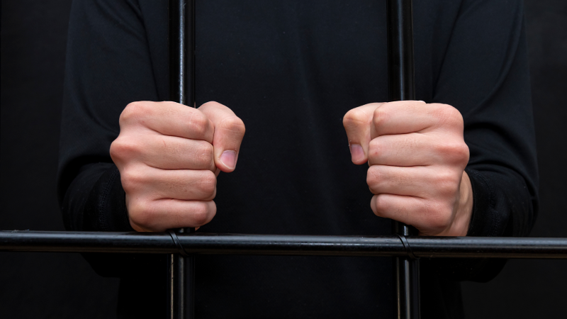 The prisoner holds his hands behind the bars in the courtroom, dark tone, selective focus.