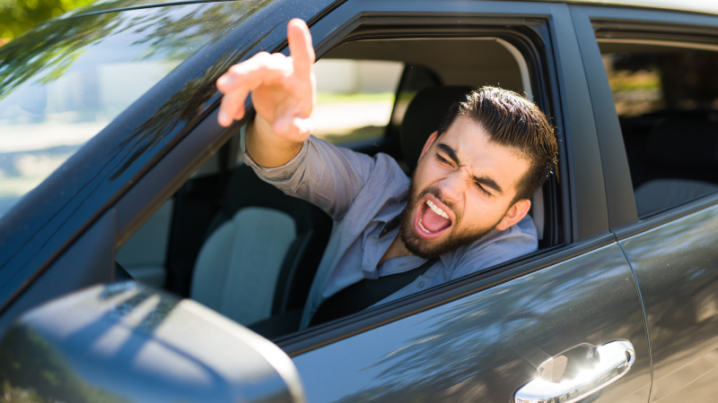 Road rage concept. Angry and aggressive young man shouting to a passing driver while arguing during a traffic jam