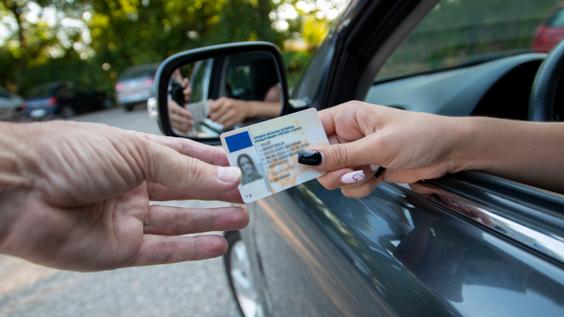 Teenager driver committed a minor offence and handing over her license to a police officer reaching towards the open window. Police officer controlling traffic on the road