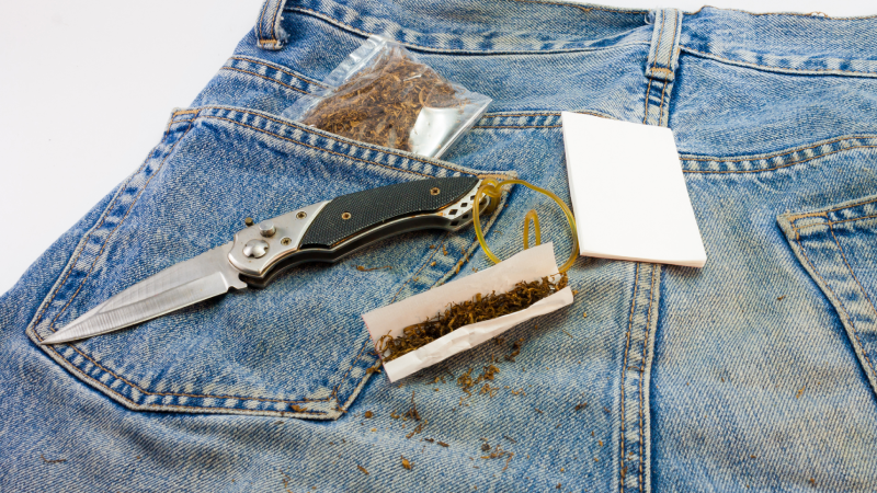 Folding knife with cigar paper, tobacco, marijuana on jeans
